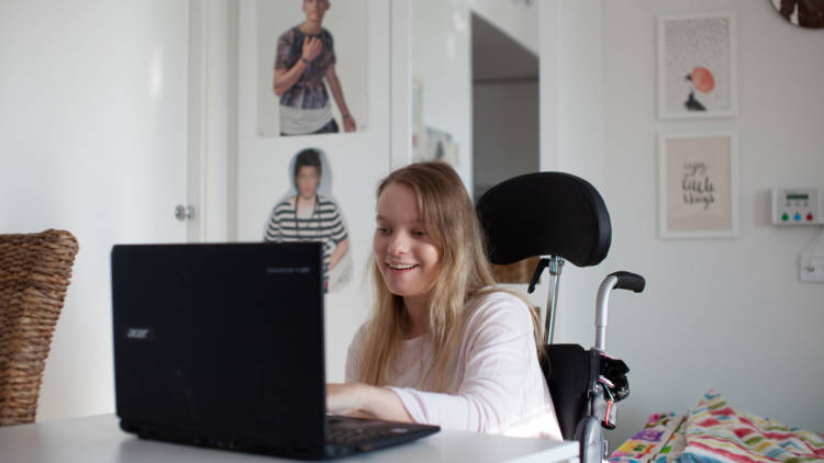 Nuori nainen pyörätuolissa tietokoneen ääressä.