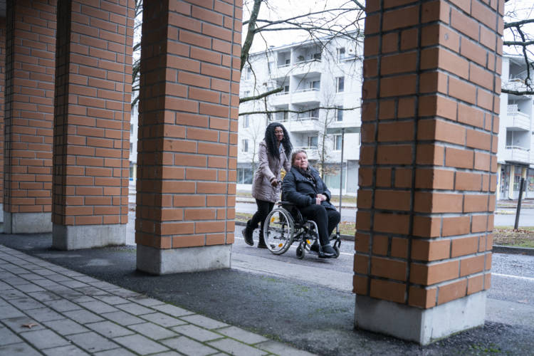 Henkilökohtainen avustaja työntää asiakasta pyörätuolissa pihalla.